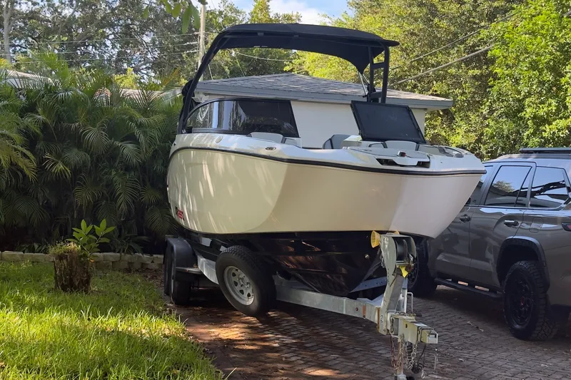 Slide: The Image of 2024 Yamaha Boats AR250 on trailer, parked in a driveway surrounded by greenery. - 18