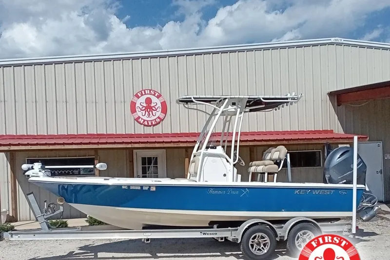 The Image of 2016 Key West 210 Bay Reef boat on trailer, parked outside a building under a cloudy sky. - 2