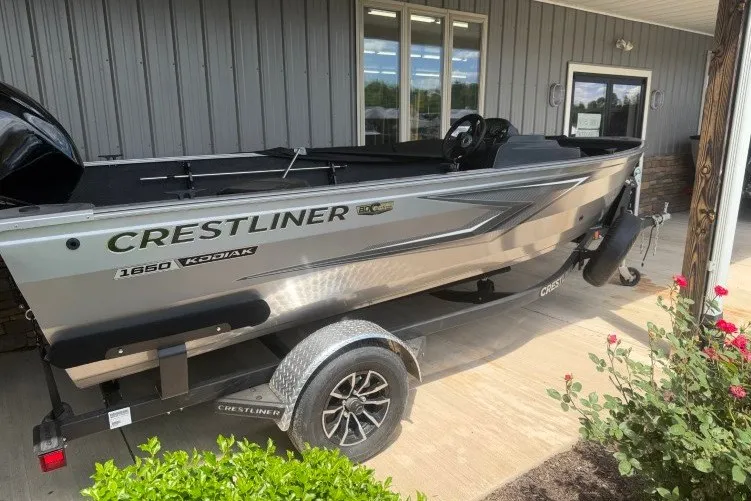 Slide: The Image of 2026 Crestliner 1650 Kodiak SC boat on trailer, parked outside a building. - 1