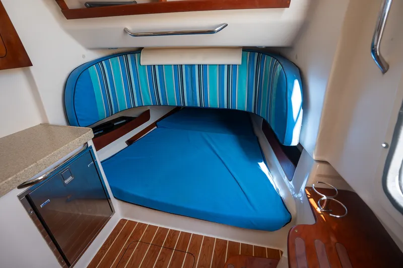 Slide: The Image of 2015 Grady-White Canyon 376 cabin interior with blue-striped bedding and compact kitchenette. - 27