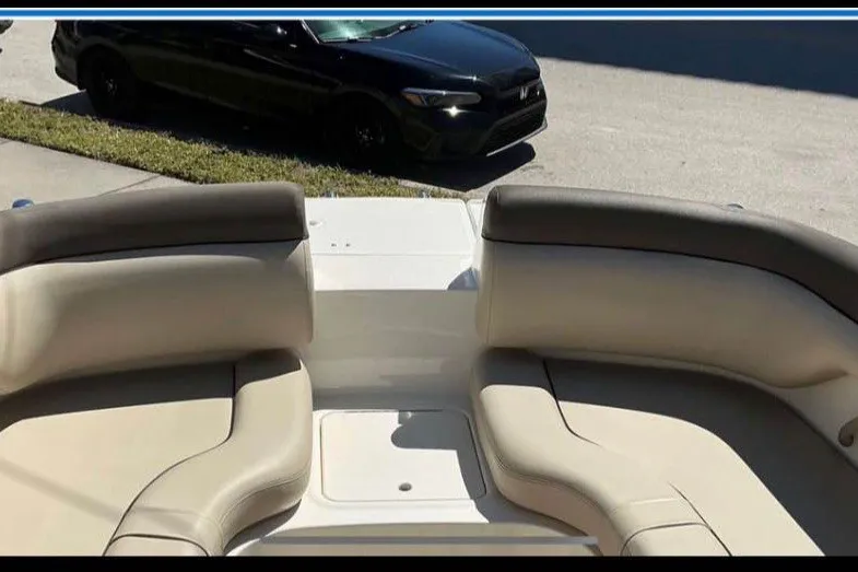 Slide: The Image of 2017 Bayliner 190 Deck Boat interior with beige seating, parked black car in background. - 7