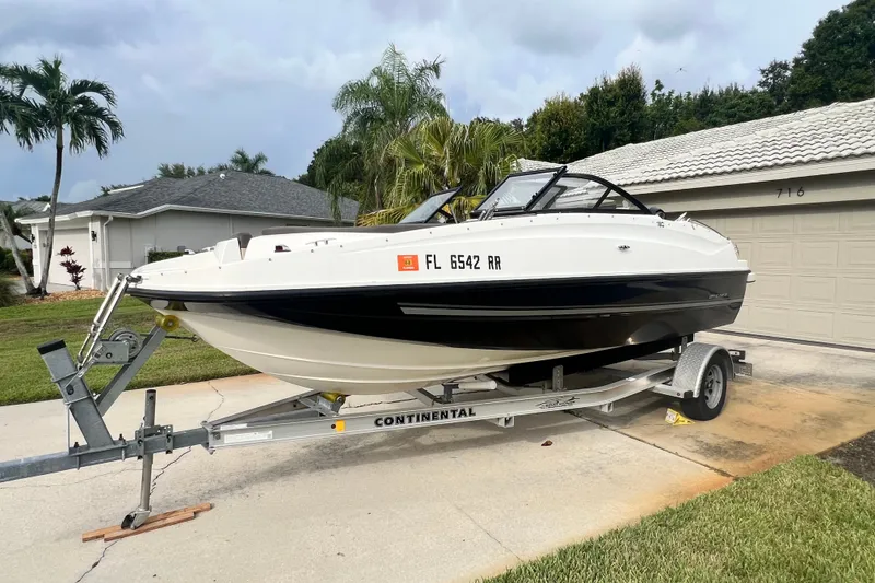 The Image of 2017 Bayliner 190 Deck Boat on trailer in residential driveway, surrounded by palm trees. - 0