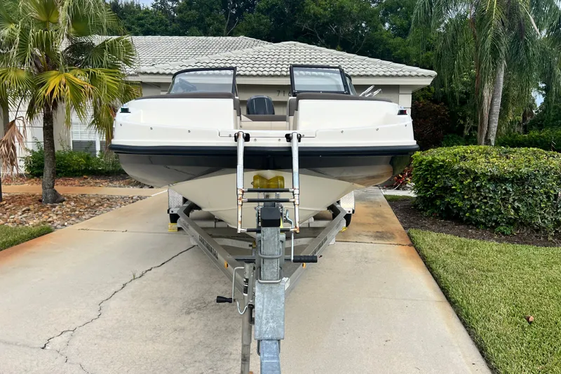 Slide: The Image of 2017 Bayliner 190 Deck Boat on trailer, parked in driveway with tropical landscaping. - 8