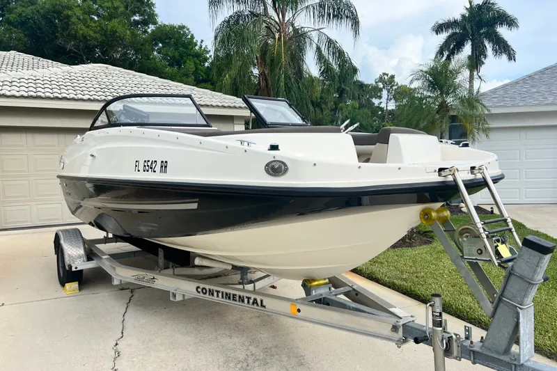 Slide: The Image of 2017 Bayliner 190 Deck Boat on trailer, parked in driveway with palm trees. - 6
