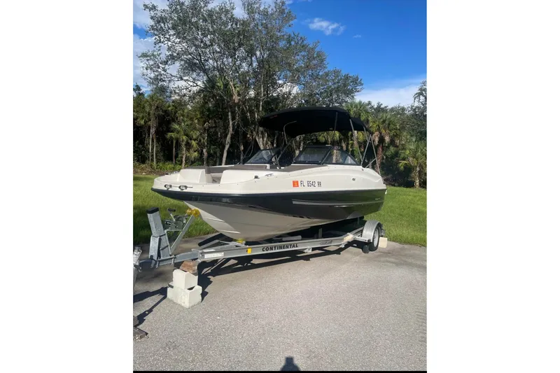 Slide: The Image of 2017 Bayliner 190 Deck Boat on trailer, parked outdoors with trees in background. - 3