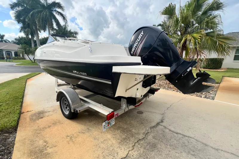 Slide: The Image of 2017 Bayliner 190 Deck Boat on trailer with Mercury outboard motor, parked in driveway. - 2