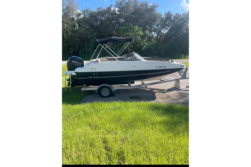 Slide: The Image of 2017 Bayliner 190 Deck Boat on trailer, parked on grass, with trees in background. - 1
