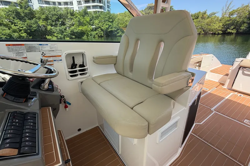 Slide: The Image of 2016 Pursuit DC 325 Dual Console helm seat with steering wheel, docked by lush greenery. - 30