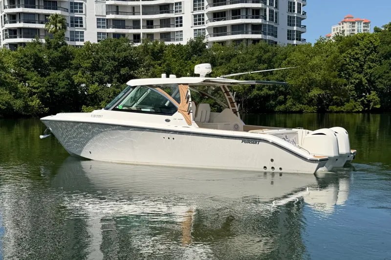 Slide: The Image of 2016 Pursuit DC 325 Dual Console boat on calm water near modern buildings. - 3