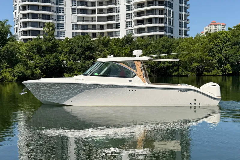 Slide: The Image of 2016 Pursuit DC 325 Dual Console boat on calm water near modern buildings. - 2