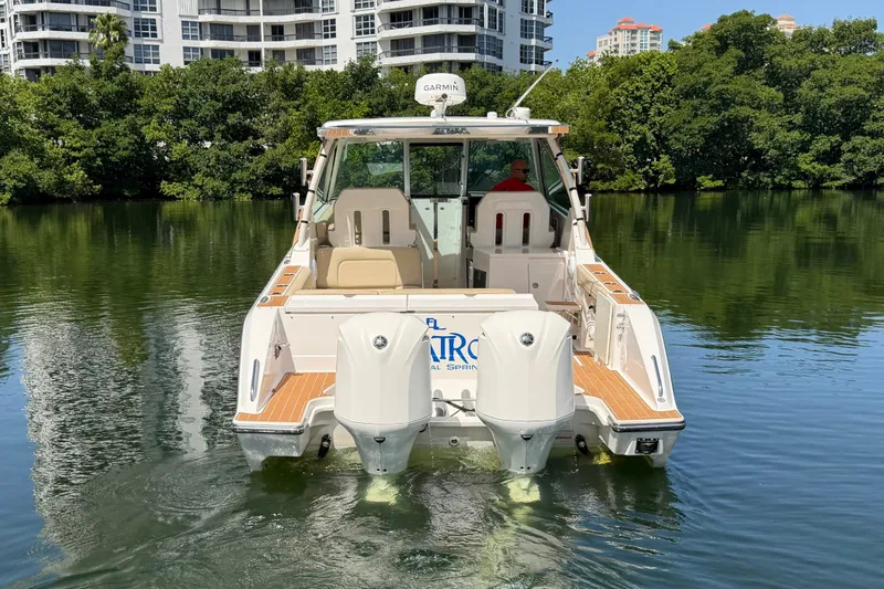 Slide: The Image of 2016 Pursuit DC 325 Dual Console boat on calm water, surrounded by greenery and buildings. - 7