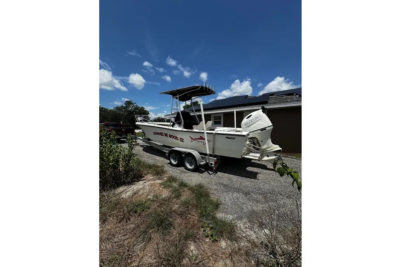 Slide: The Image of 1977 Mako 235 boat with Suzuki outboard motor on a trailer, parked outdoors. - 3