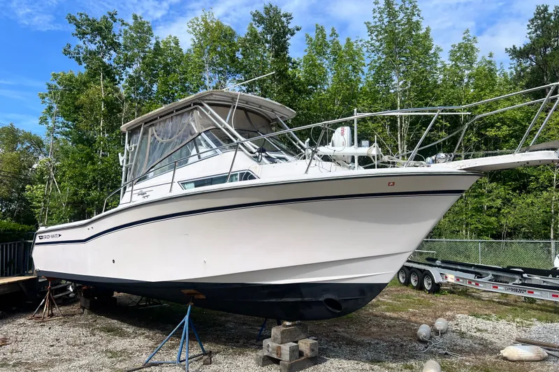 The Image of 1996 Grady-White Marlin 300 boat on stands, surrounded by trees and a trailer. - 1
