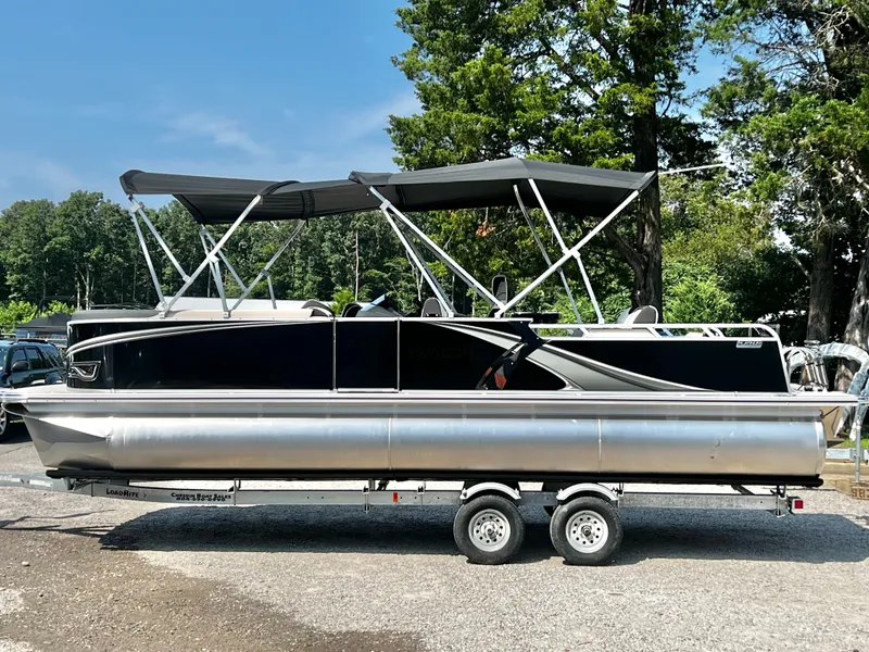 Slide: The Image of A sleek pontoon boat with a black hull and gray sun canopies, parked on a trailer. - 6