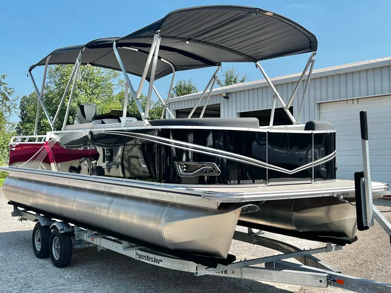 The Image of A sleek pontoon boat with a black hull and dual bimini tops, parked on a trailer. - 1