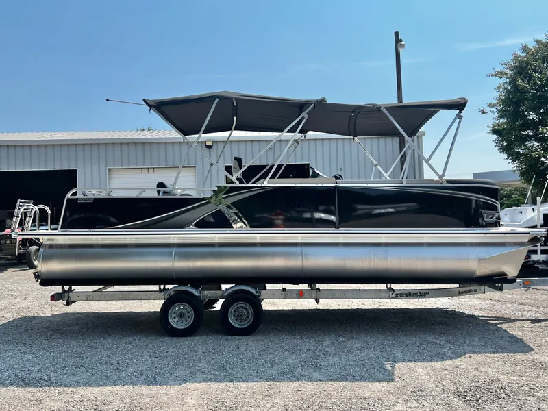 Slide: The Image of A black Avalon LSZ 25' Entertainer pontoon boat on a trailer in front of a building. - 2