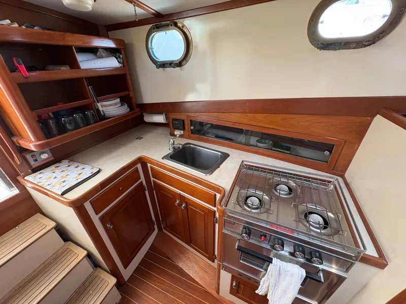 Slide: The Image of The galley of a 1988 Jarvis Newman 32 with wooden cabinets and a gas stove. - 19