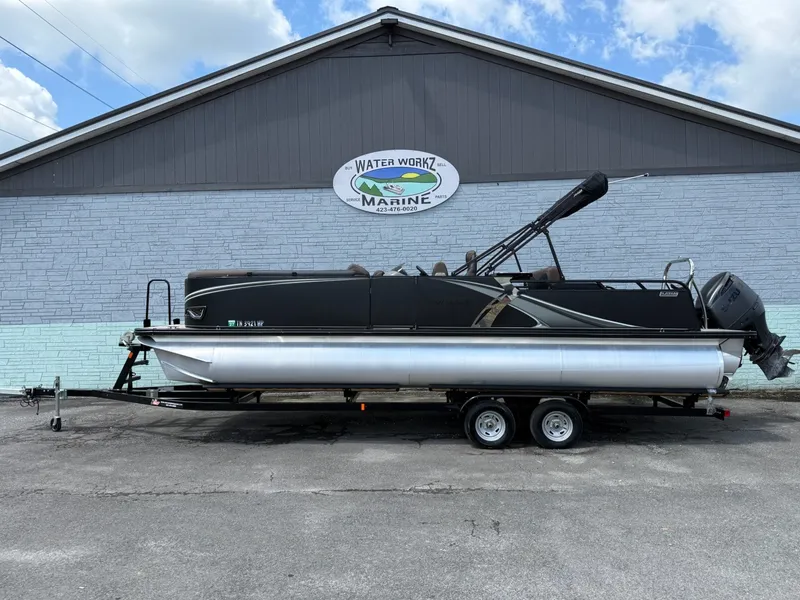 The Image of An Avalon 2585 LSZ Entertainer pontoon boat on a trailer in front of a building with a sign. - 1