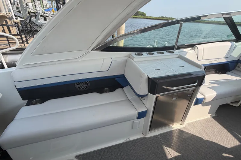 Slide: The Image of 2020 Formula 330 Crossover Bowrider I/O interior with seating and mini-fridge, docked by water. - 9