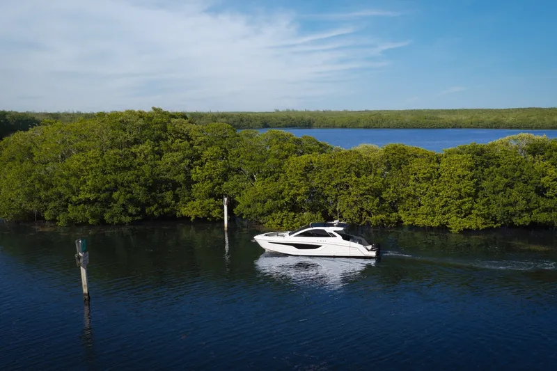Slide: The Image of 2021 Cruisers Yachts 42 GLS OB navigating serene waters near lush greenery. - 32