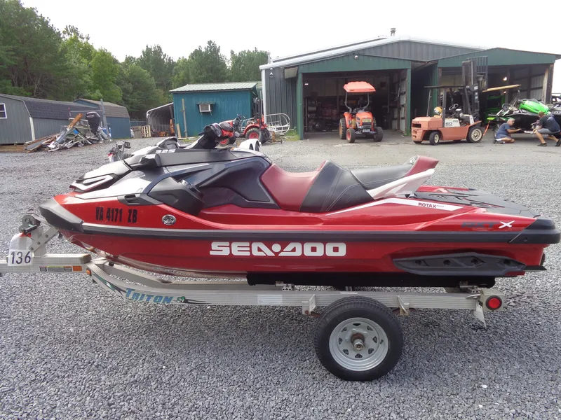 The Image of A red 2024 Sea-Doo RXT-X 325 sits on a trailer in a gravel lot. - 1