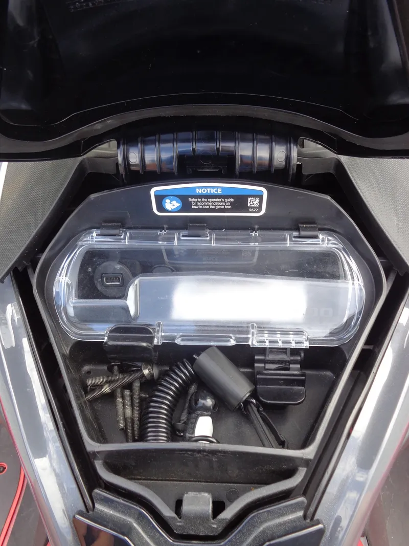 Slide: The Image of An open storage compartment with screws and cables in a 2024 Sea-Doo RXT-X 325 Tech Package. - 21