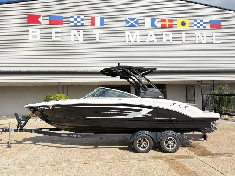 The Image of A black 2021 Chaparral 23 SSi boat on a trailer in front of a building with flags. - 1