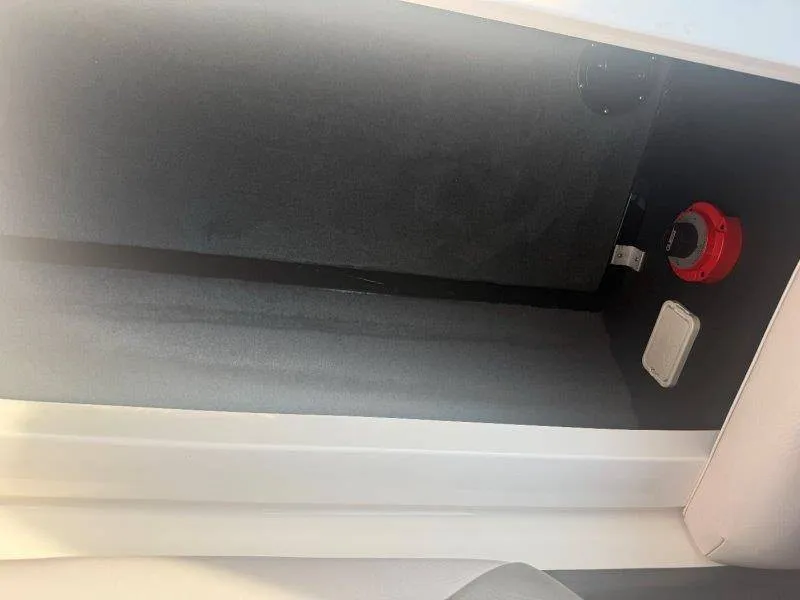 Slide: The Image of An empty storage compartment inside a boat with gray carpeting and a red switch. - 30