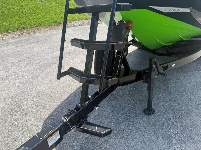 Slide: The Image of A green boat on a trailer with a black frame and steps, on a paved area. - 13