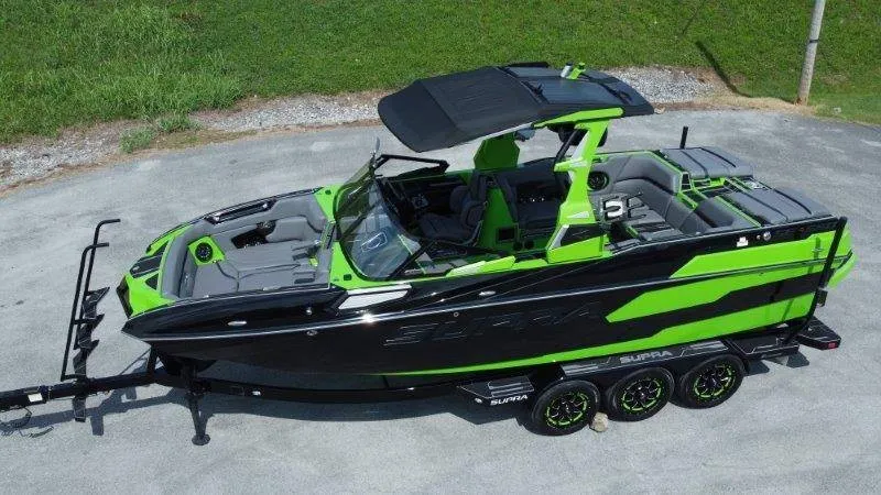 Slide: The Image of A 2023 Supra SE 550 boat in black and green on a trailer, ready for transport. - 2