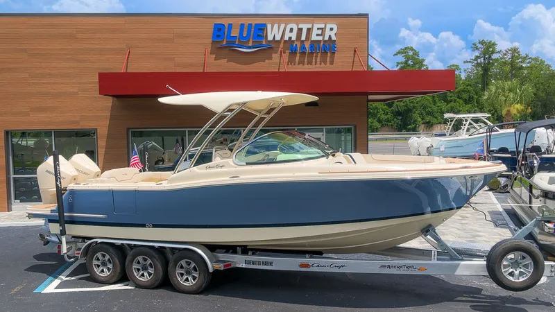 The Image of A 2022 Chris-Craft Calypso 27 boat on a trailer in front of a marine store. - 1