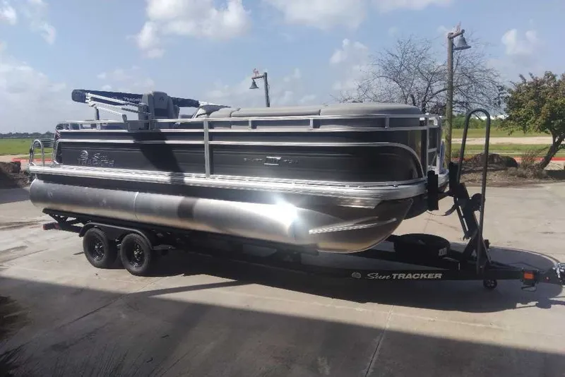The Image of 2027 Sun Tracker SportFish 20 DLX pontoon boat on trailer, parked outdoors. - 0