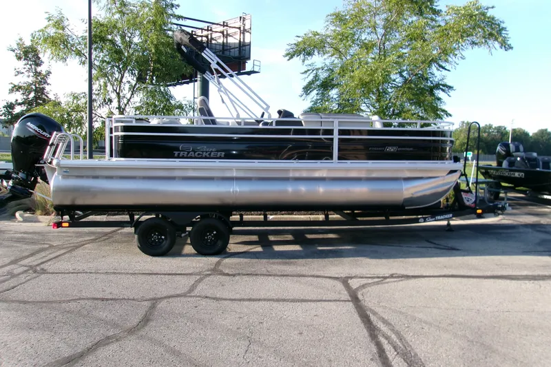 The Image of 2027 Sun Tracker Fishin' Barge 22 DLX pontoon boat on trailer, parked outdoors. - 0