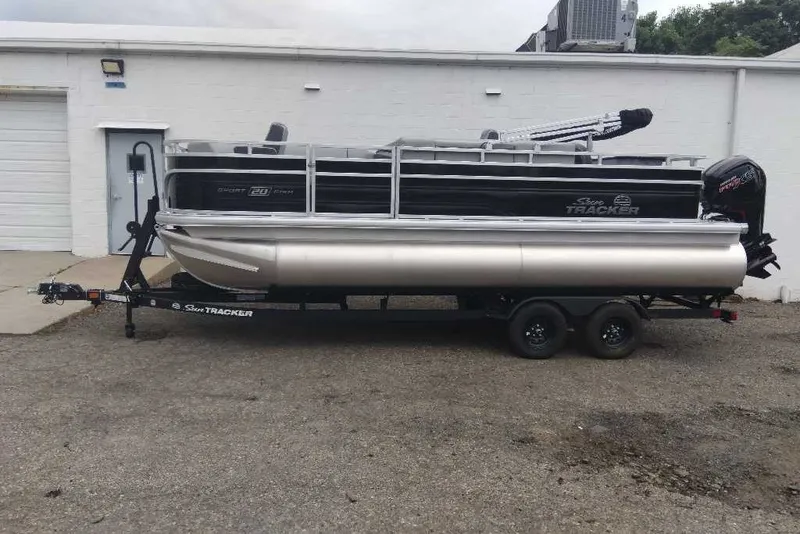 The Image of 2027 Sun Tracker SportFish 20 DLX pontoon boat on trailer, parked outdoors. - 0