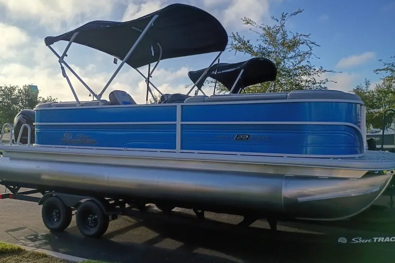 The Image of 2027 Sun Tracker Party Barge 22 DLX pontoon boat with canopy, parked on trailer. - 0