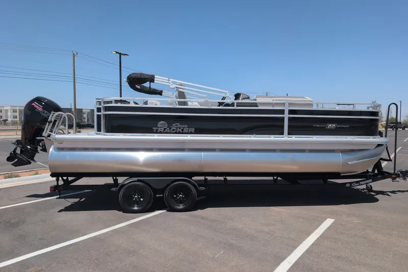 The Image of 2027 Sun Tracker Fishin' Barge 22 DLX pontoon boat on trailer in parking lot. - 0