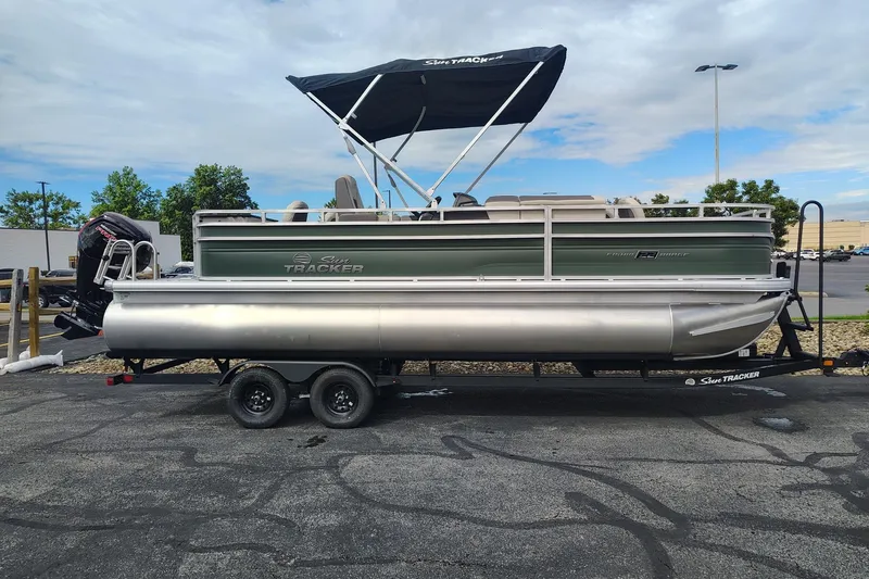The Image of 2027 Sun Tracker Fishin' Barge 22 DLX pontoon boat on trailer, parked outdoors. - 0