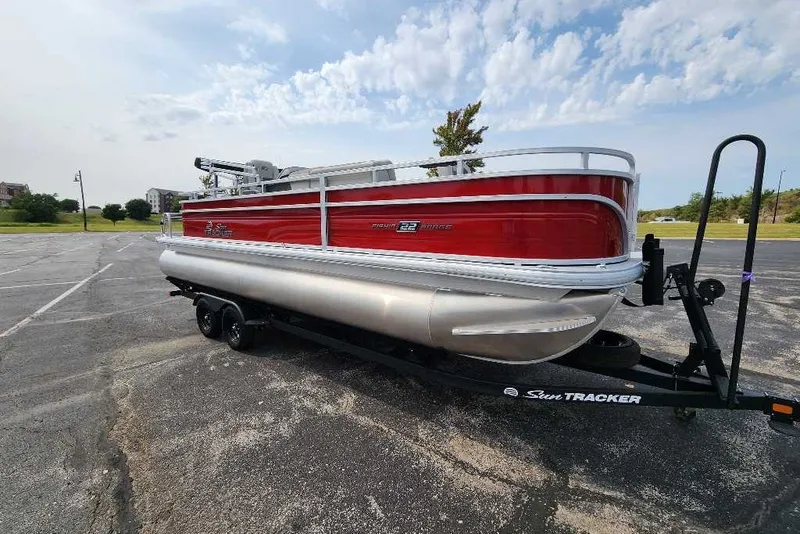 The Image of 2027 Sun Tracker Fishin' Barge 22 DLX pontoon boat on trailer in parking lot. - 0