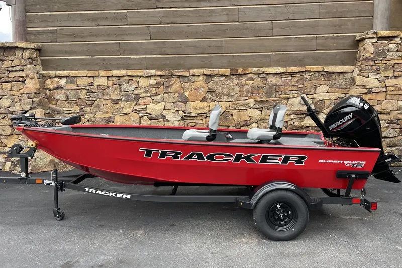 The Image of Red 2027 Tracker Super Guide V-16 T boat on trailer, parked by stone wall. - 0