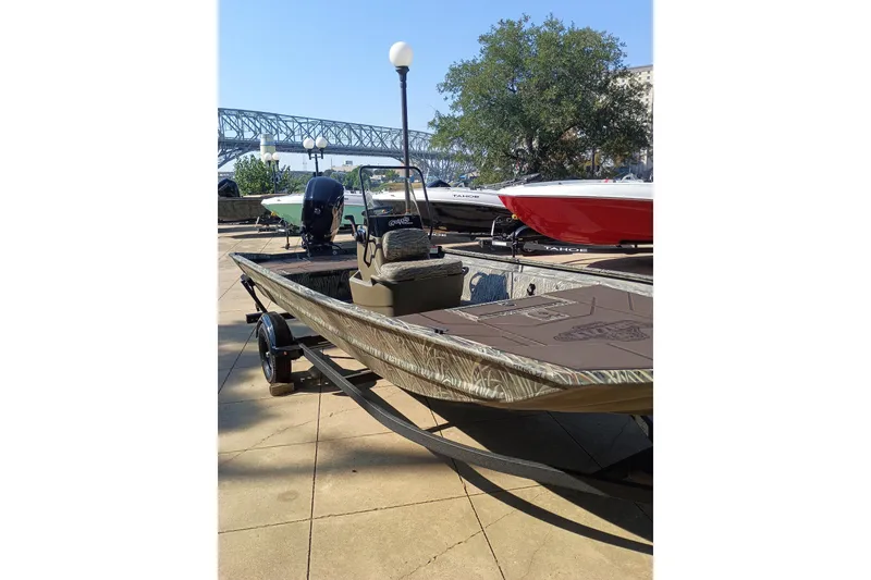 The Image of 2027 Tracker Grizzly 1860 CC boat on trailer, outdoor display with bridge and trees. - 0