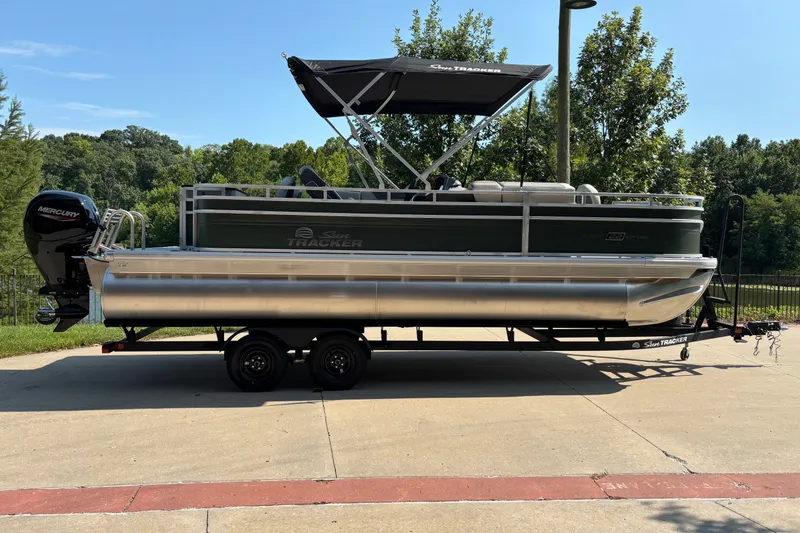 The Image of 2027 Sun Tracker Fishin' Barge 22 DLX pontoon boat on trailer, parked outdoors. - 0