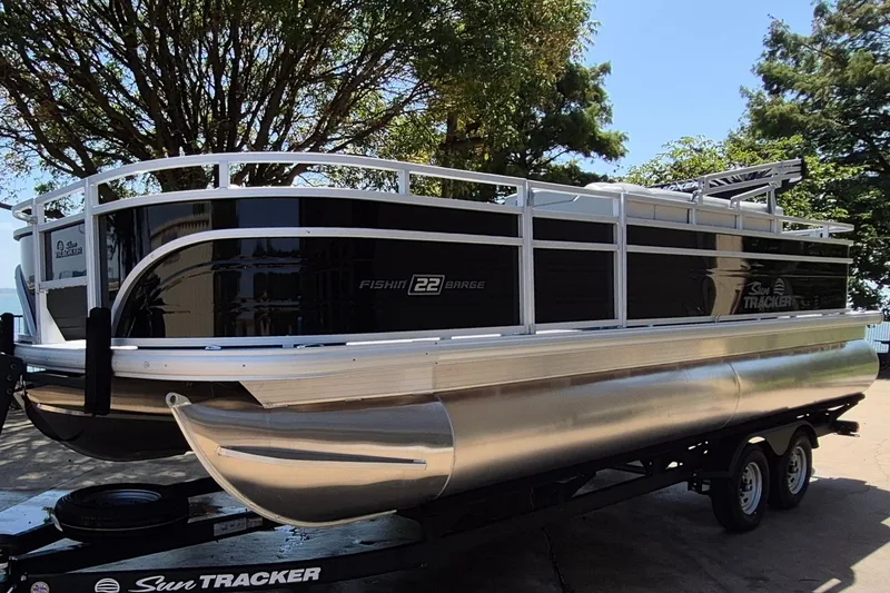 The Image of 2027 Sun Tracker Fishin' Barge 22 DLX pontoon boat on trailer, parked outdoors. - 0