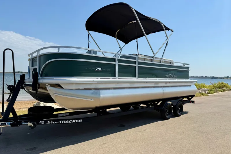 The Image of 2027 Sun Tracker Fishin' Barge 22 DLX pontoon boat on trailer by a lake. - 0
