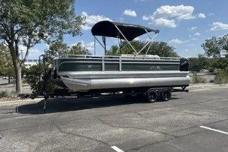 The Image of 2027 Sun Tracker Fishin' Barge 22 DLX pontoon boat on trailer, parked outdoors. - 0