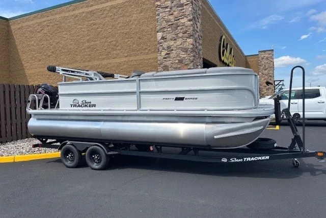 The Image of 2027 Sun Tracker Party Barge 20 DLX pontoon boat on trailer, parked outside a store. - 0
