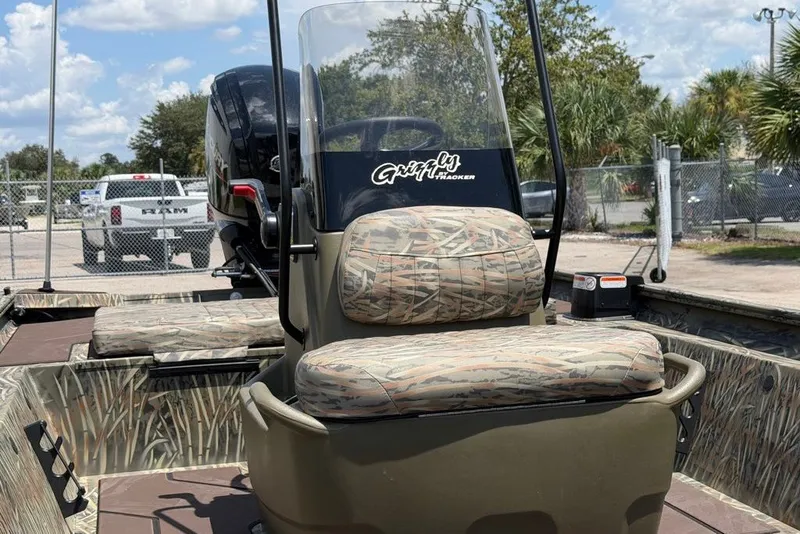 Slide: The Image of 2027 Tracker Grizzly 1860 CC boat with camo seats and windshield, parked outdoors. - 70
