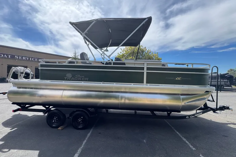 The Image of 2027 Sun Tracker Fishin' Barge 22 DLX pontoon boat on trailer, parked outdoors. - 0