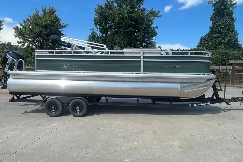 The Image of 2027 Sun Tracker Fishin' Barge 22 DLX pontoon boat on trailer, parked outdoors. - 0