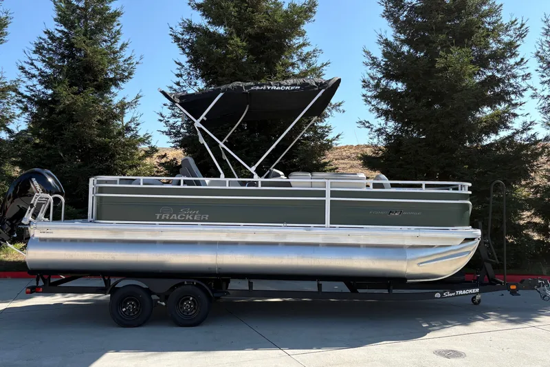 The Image of 2027 Sun Tracker Fishin' Barge 22 DLX pontoon boat on trailer, parked outdoors. - 0