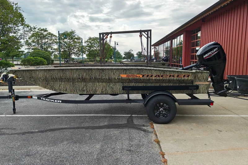The Image of 2027 Tracker Grizzly 1756 T Marsh boat on trailer, parked outdoors near red building. - 1